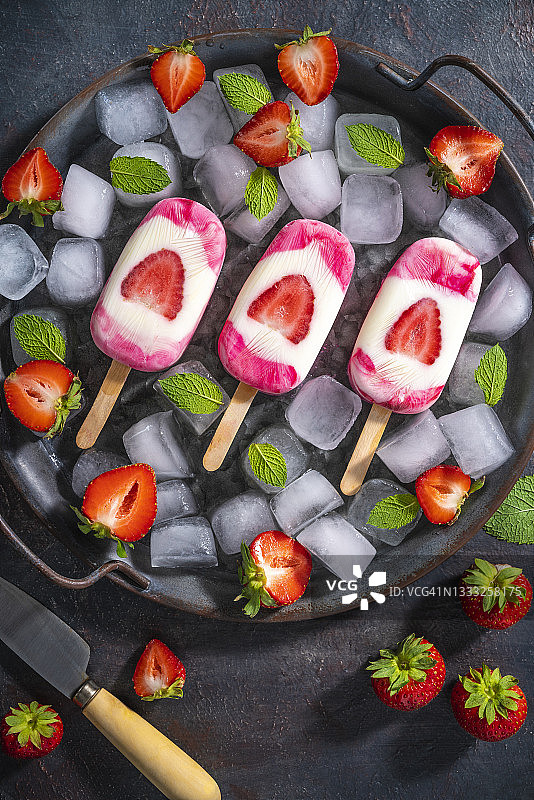 草莓自制冰棒，薄荷叶放在冰块上，平底锅深色背景图片素材