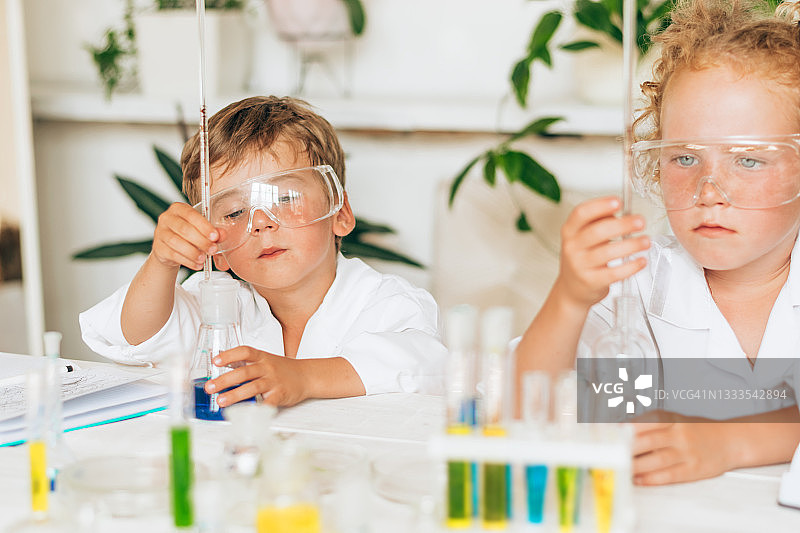 一群穿着白色制服的严肃的小男孩和小女孩在实验室里做化学实验。回到学校的概念。年轻的科学家。自然科学。儿童的学前和学校教育图片素材
