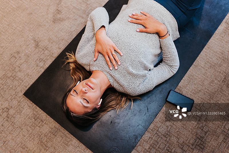 一个女人躺在家里的瑜伽垫上冥想图片素材