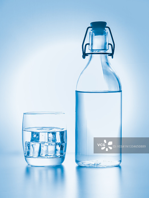 玻璃杯与冰和水瓶在天蓝色的背景图片素材