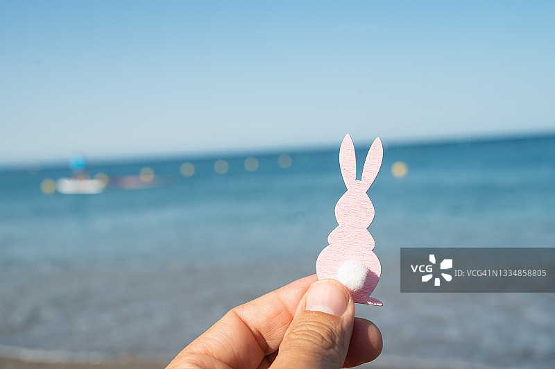 在海滩的岸边，一个人手里拿着一个复活节兔子的小雕像。图片素材