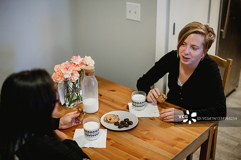 两个成年妇女享受友谊和牛奶和饼干一起在家庭厨房图片素材