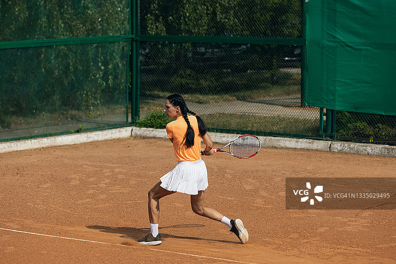 美丽的年轻女运动员，职业网球运动员，带着球拍在夏天的粘土网球场练习。图片素材