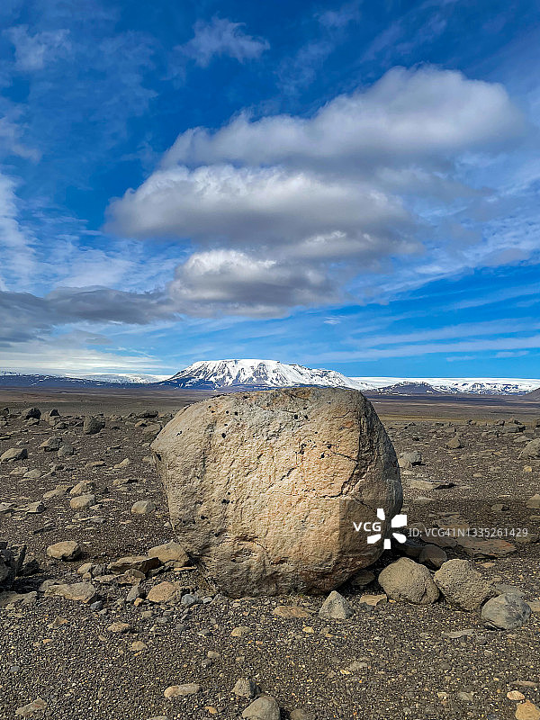 巨大的巨石在巨大的贫瘠的火山岩上的特写镜头，覆盖着白雪覆盖的山脉和深蓝色的引人注目的天空。图片素材