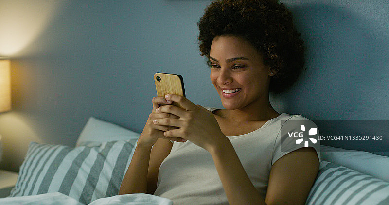 一名年轻女子晚上躺在床上使用手机图片素材