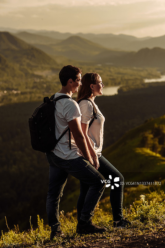 两个年轻的男男女女背着背包在山顶上愉快地欣赏着山谷的景色。旅行和旅行的概念图片素材