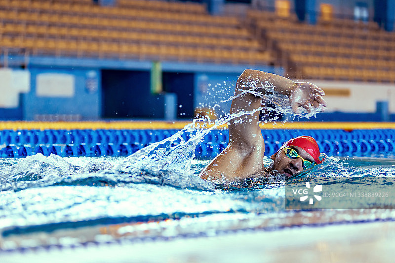 在室内游泳池训练期间，专业男性游泳运动员戴着游泳帽和泳镜进行运动和动作。健康的生活方式，动力，能量，运动理念图片素材