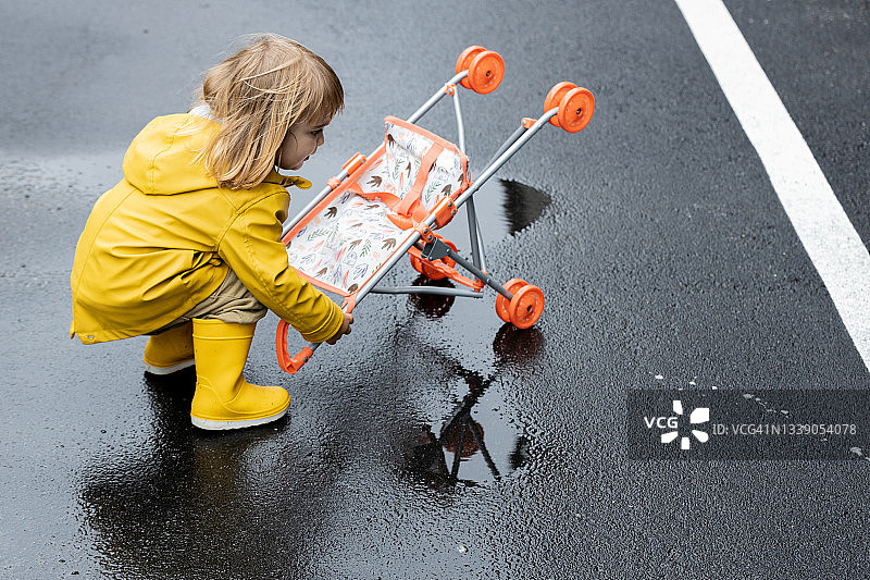 下雨天，一个小女孩推着一辆玩具婴儿车在外面玩。图片素材