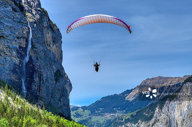 在一个阳光明媚的春天，滑翔伞飞过山坡。假日休闲体育活动图片素材