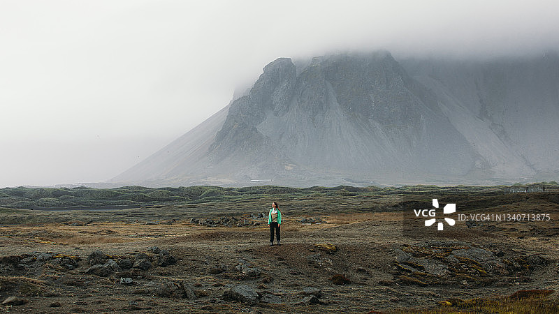 在冰岛的黑沙丘海滩上，一名女游客被令人敬畏的山景包围着图片素材