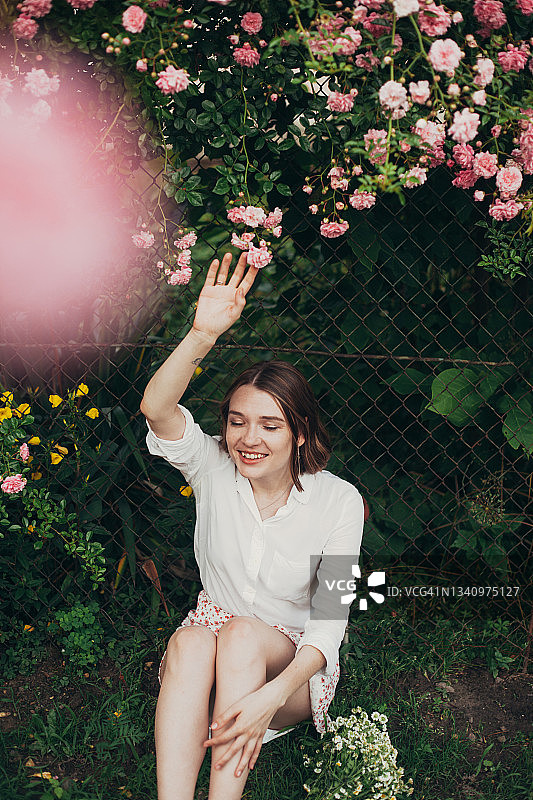 快乐的年轻女子在粉红玫瑰的花园里度过夏日图片素材