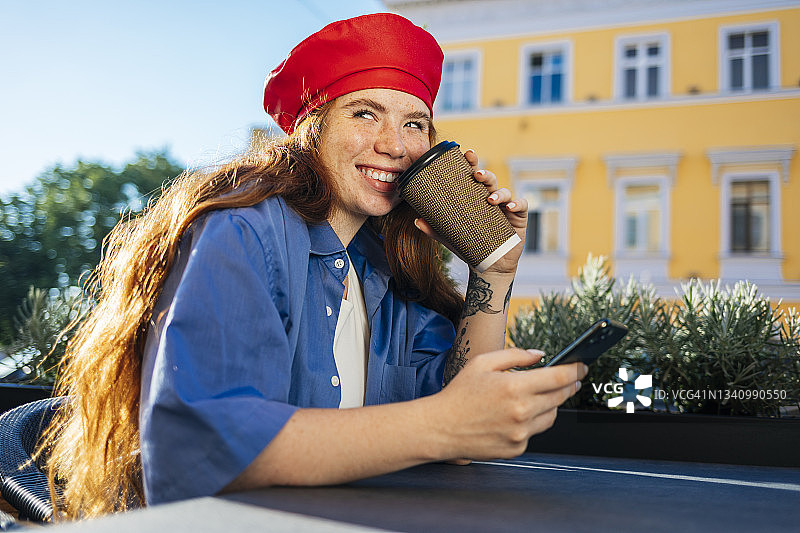 微笑的年轻女子拿着手机在路边咖啡馆喝咖啡图片素材