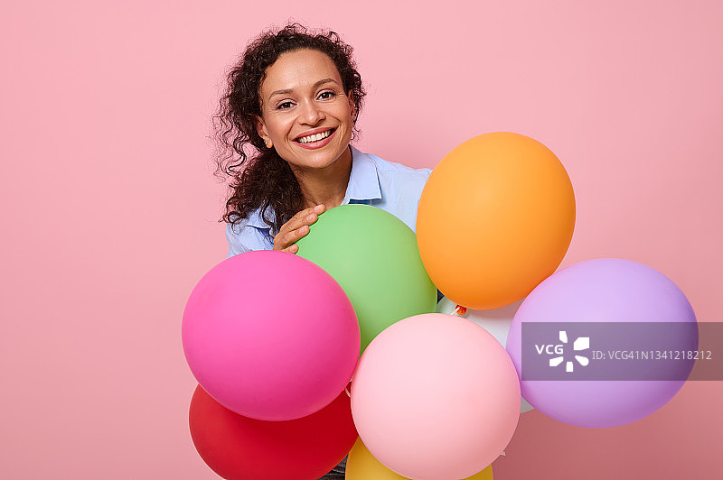 美丽的惊人的非洲裔美国卷发女人的脸肖像与牙齿微笑站在彩色气球孤立在粉红色明亮的背景与复制空间图片素材