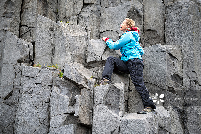 一名成熟女子在冰岛瑞尼斯法拉黑沙滩上攀登加达玄武岩柱。图片素材