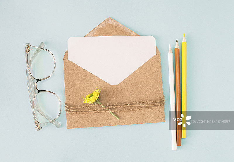 棕色纸工艺信封与空白的白色卡片，铅笔，眼镜和花的蓝色背景图片素材