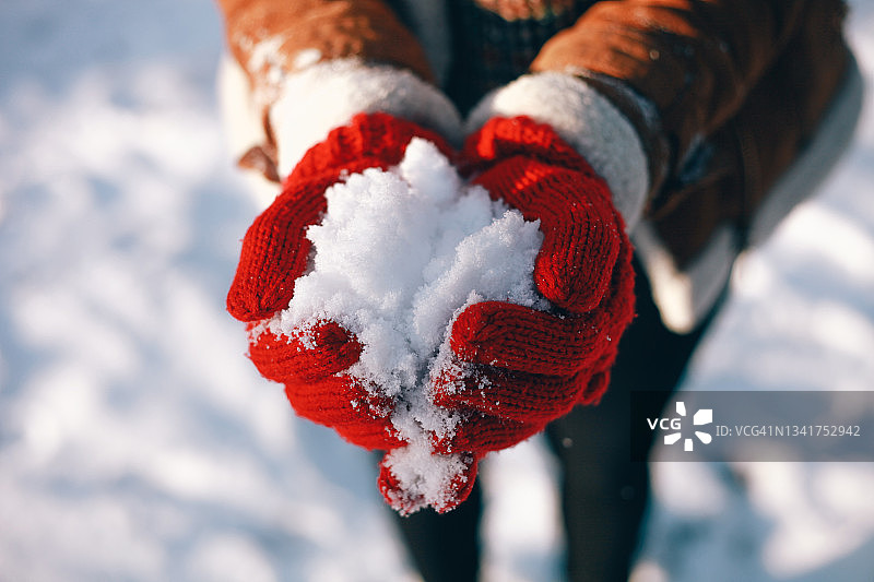 在阳光明媚的冬日里，戴着红色针织手套的女性手握着雪在户外玩耍图片素材