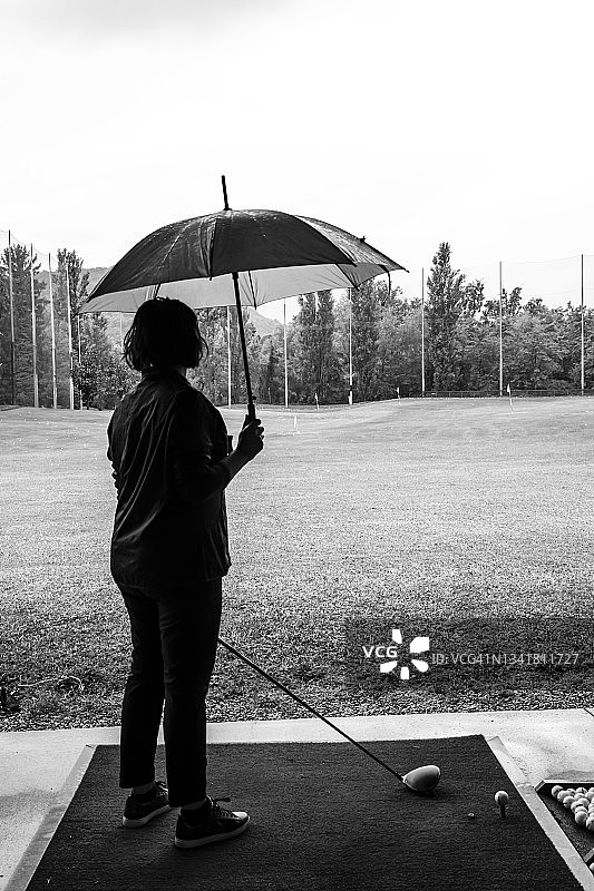 下雨天，高尔夫球手在练习场手持高尔夫球棒和雨伞图片素材