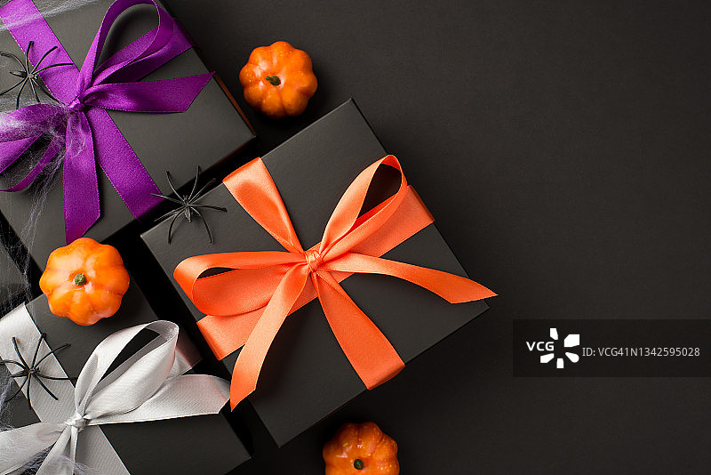 顶部视图的照片万圣节组成三个黑色礼品盒紫罗兰橙和白色丝带蝴蝶结小南瓜蜘蛛和蜘蛛网孤立的黑色背景与copyspace图片素材