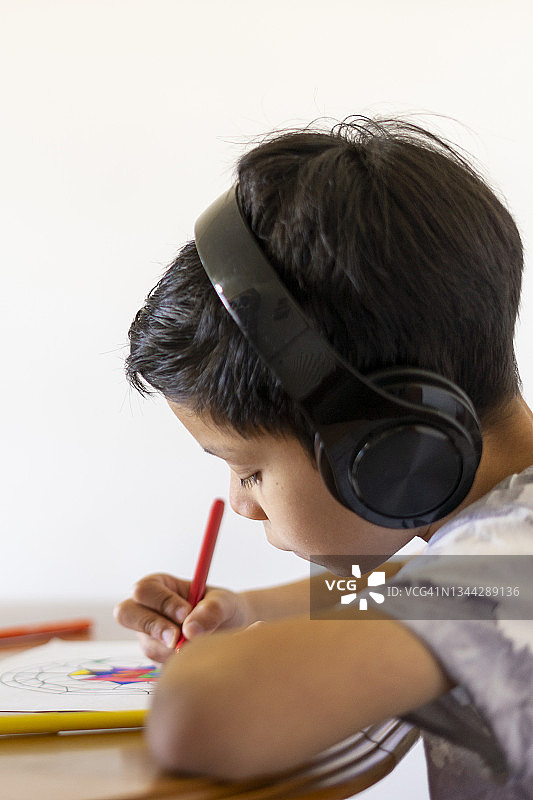 男孩在家里用彩笔画画，戴着耳机听音乐图片素材
