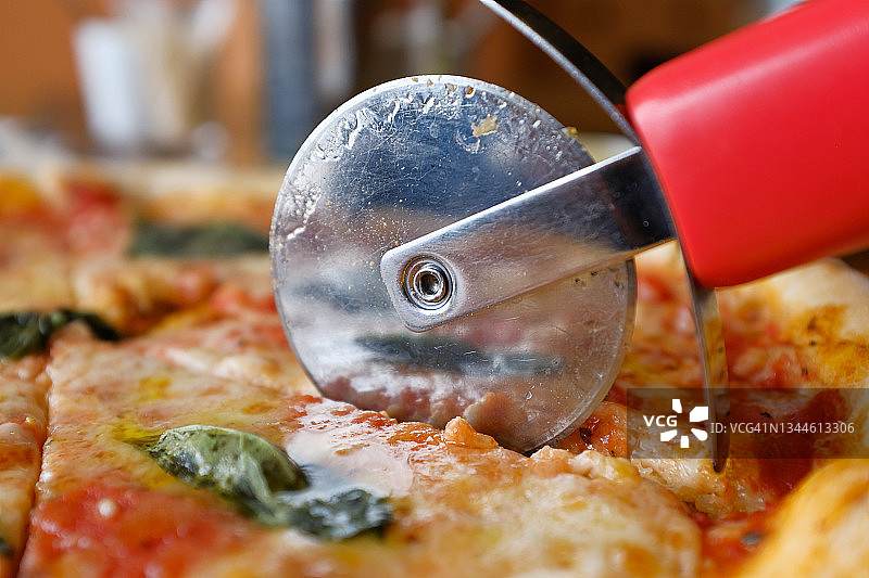 在咖啡馆或快餐店里，一位女士用马苏里拉奶酪、番茄、罗勒切了一块素食披萨。美味的意大利美食。切披萨玛格丽塔在木板或架子上。美味不健康的午餐，零食。图片素材