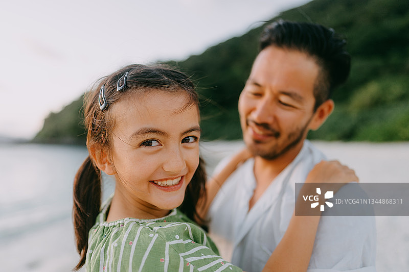 快乐的年轻女孩拥抱她的父亲在海滩日落，日本图片素材