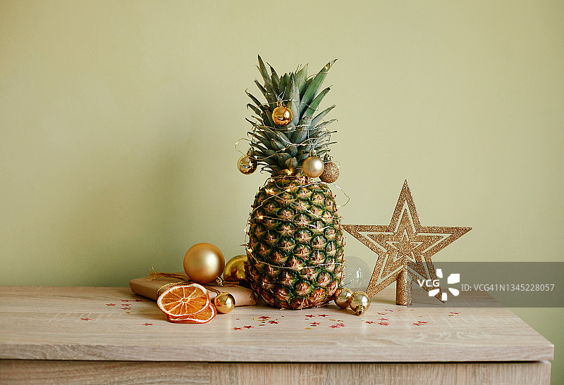 圣诞节的节日家居装饰。用金色的小玩意装饰的菠萝，还有桌子上的圣诞装饰品。热带圣诞节和新年。图片素材
