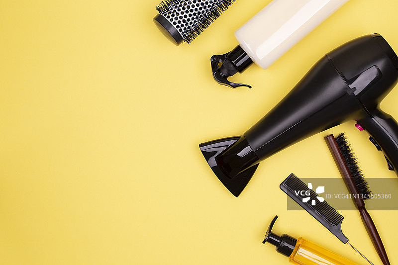 黑色的美发工具:电吹风，梳子，黄色背景上的喷雾剂，放文字的地方，平放。图片素材