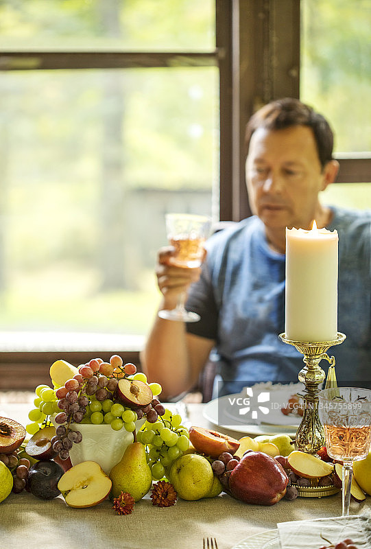 男人拿着一杯葡萄酒坐在用新鲜水果装饰的秋天餐桌上。图片素材