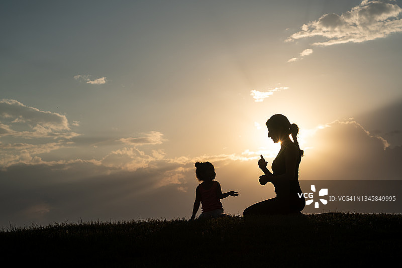 成年妇女和小女孩在夕阳下做瑜伽练习的剪影图片素材