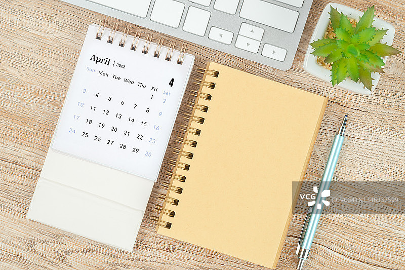 2022年四月月历桌，顶视图日历和笔，笔记本在木桌背景。图片素材