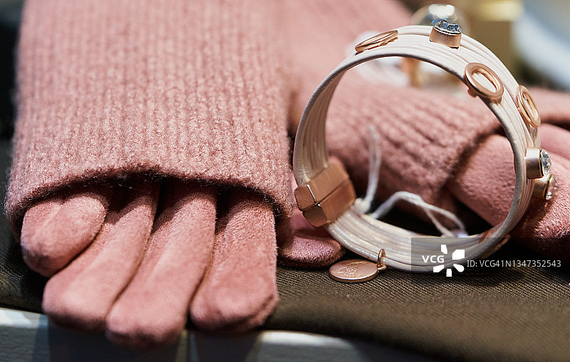 近距离观察商店橱窗里的玫瑰色毛衣袖子、手套和手镯。一件玫瑰色毛衣、一双手套和一只白色手镯陈列在一家商店的橱窗里。图片素材