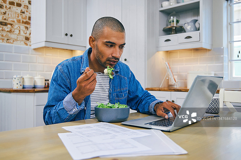 一个年轻人一边在家工作一边用笔记本电脑吃健康沙拉图片素材