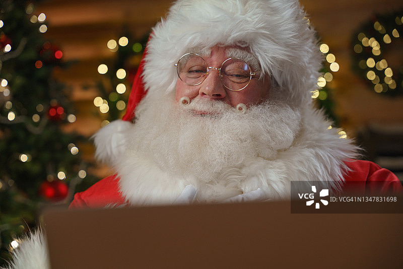 微笑的圣诞老人，看着他面前的笔记本电脑图片素材