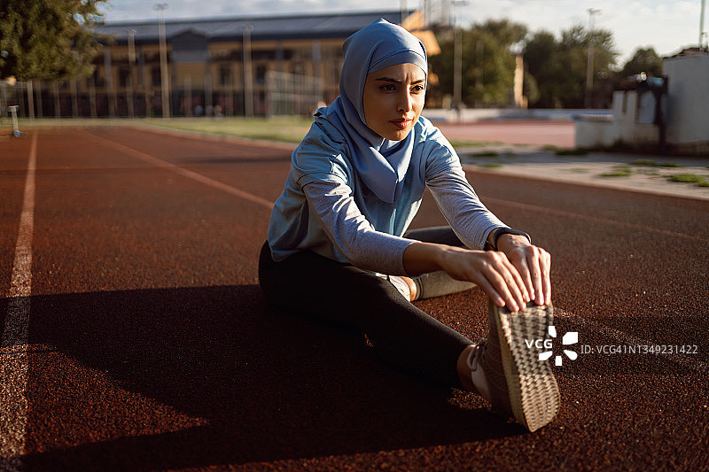 女运动员戴头巾，在进行田径训练前伸展双腿图片素材