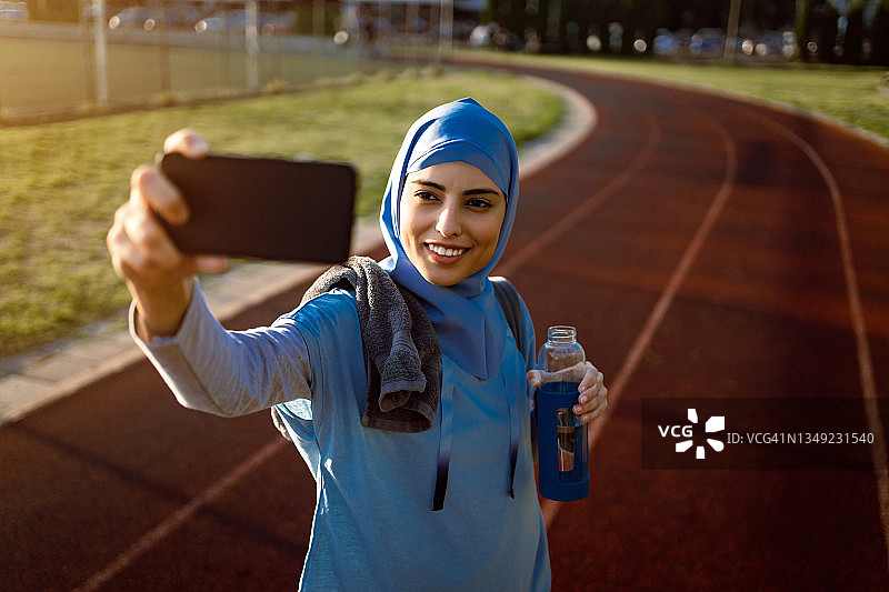微笑的穆斯林女运动员在跑道上用手机自拍图片素材