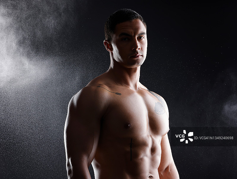 一名运动青年男子赤裸上身，在黑暗背景下摆姿势图片素材