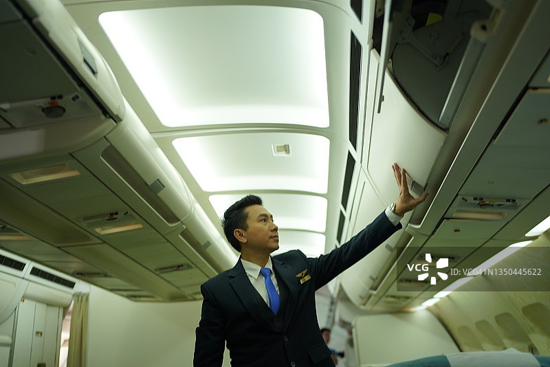 自信的亚洲男性飞行员穿着制服，站在飞机的副驾驶座位上。图片素材