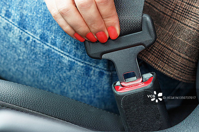 女用红色指甲的手在汽车特写系安全带。图片素材