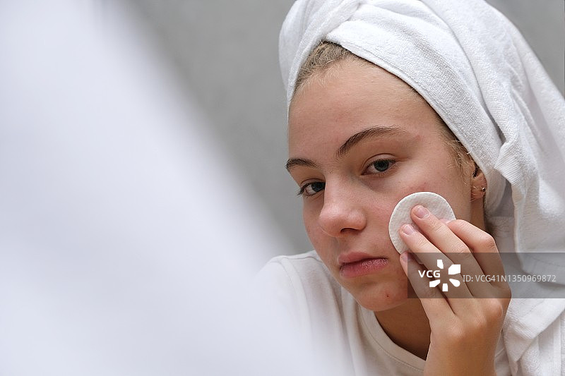 一个十几岁的女孩在镜子旁边用棉花擦脸。青春期面部皮肤护理。图片素材