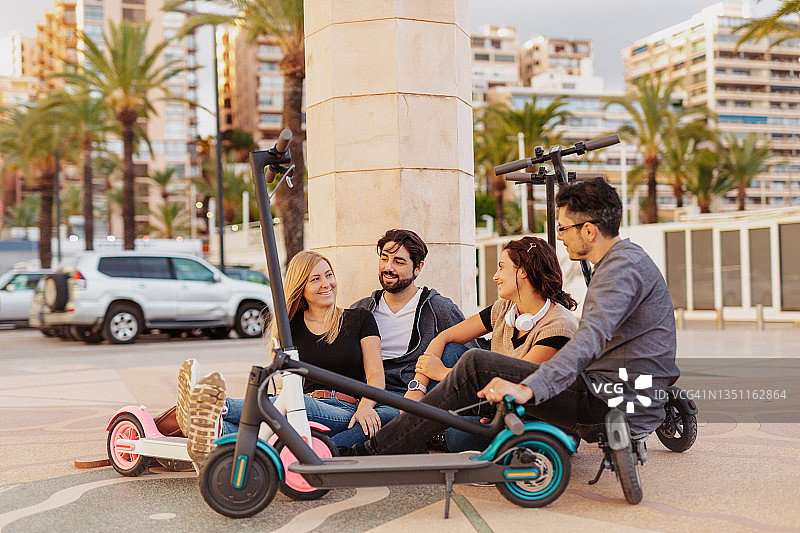 四个面带微笑的年轻人坐在摩托车旁边的地板上图片素材