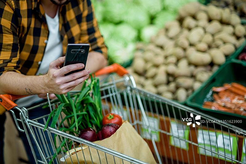 年轻英俊的男子在超市买菜时用智能手机图片素材