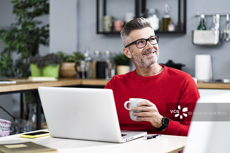带着笔记本电脑的微笑男人在家喝咖啡图片素材
