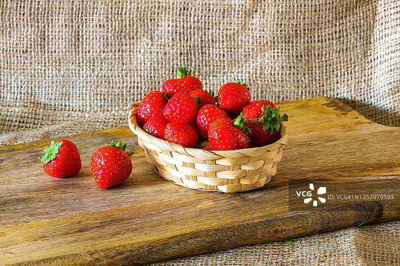 新鲜草莓装在柳条篮子里，放在旧木板上。图片素材