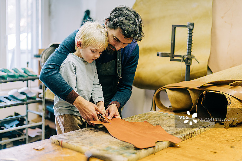 工匠和他可爱的小男孩在制作皮革表带。图片素材