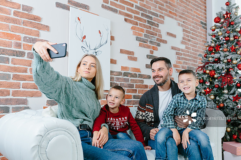 年轻的家庭用手机视频通话，快乐和微笑，丈夫妻子和你的兄弟们问候朋友们新年和圣诞节假期图片素材