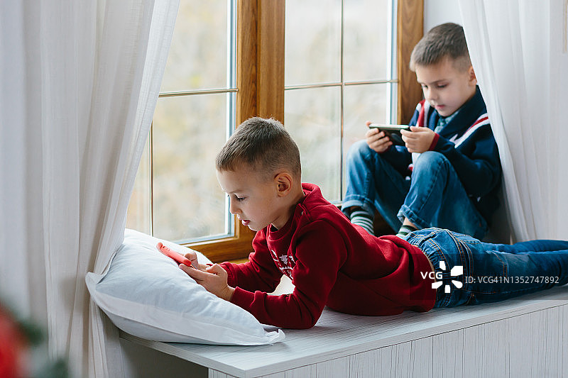 两个小男孩坐在公寓的窗台上玩手机图片素材