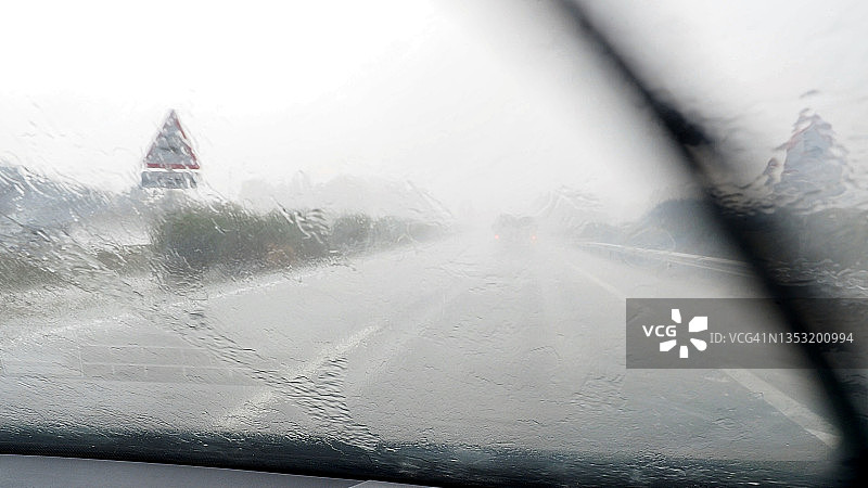 汽车视角驾驶，雨滴在汽车的挡风玻璃上行驶在高速公路上。图片素材