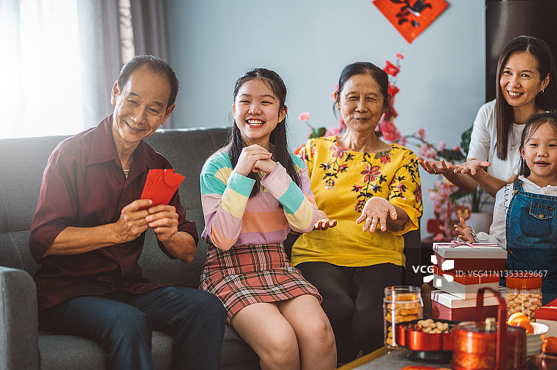 欢乐的亚洲家庭三代欢聚在客厅庆祝中国新年，享受传统美食图片素材