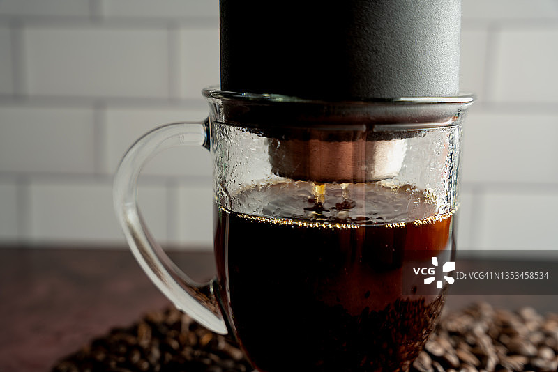 透明的玻璃咖啡杯下的倒在咖啡机作为新鲜的咖啡滴到杯子上一堆新鲜烤全豆咖啡图片素材