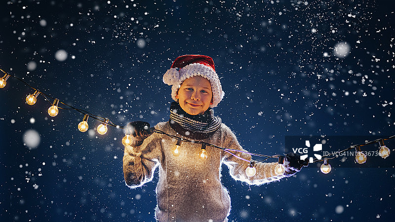 一个快乐的男孩在圣诞节与童话灯在雪图片素材